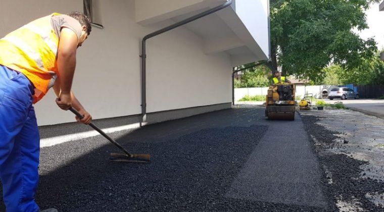 Kézi aszfaltozás gereblyével ház fala mellett, henger a háttérben
